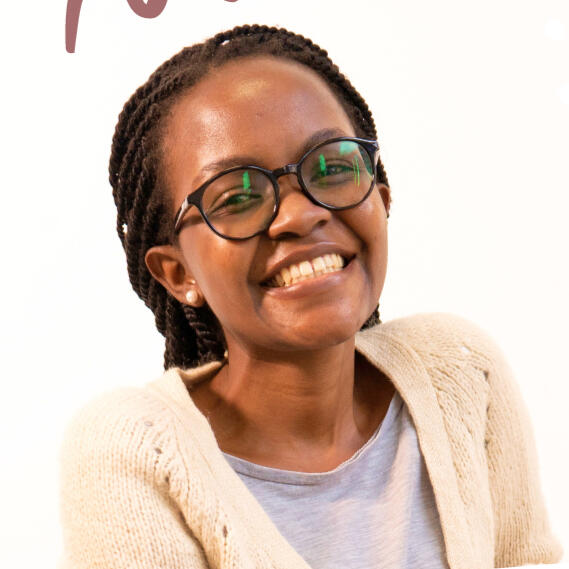 Jennifer Kyalo smiling facing the camera. Wearing spectacles, pearl earrings, grey round neck top and cream coloured sweater